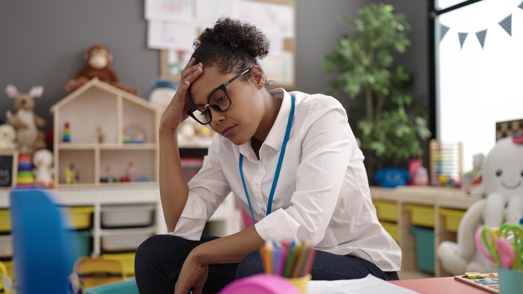 African american woman teacher overworked collecting toys at kindergarten
