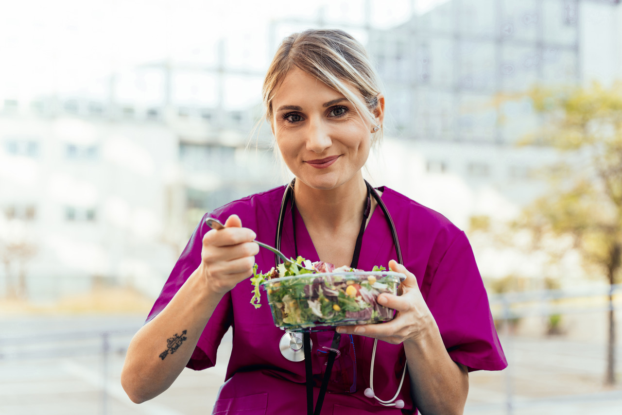 Nurse eating a salad with stethoscope around her neck sitting outside