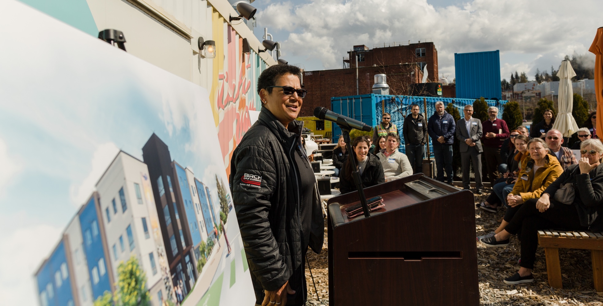 Woman giving a speech at a podium, the Millworks building mockup is beside her